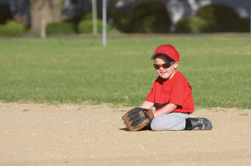 Little boy sitting in dirt during baseball game holding glove