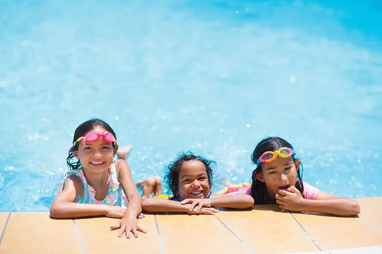 3 girls in the pool on the edge smiling.