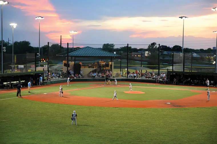 Youth baseball game playing at night with a pretty sunset