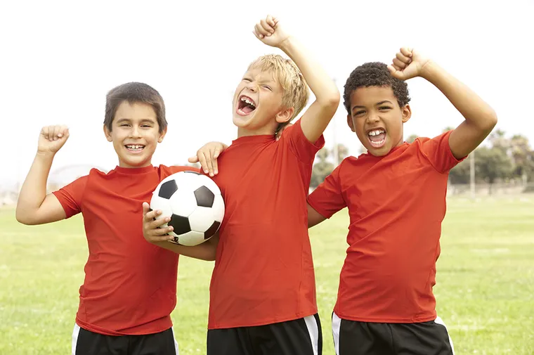 Three boys celebrating with a soccer ball