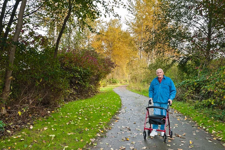 Older gentleman walking with walker through park.